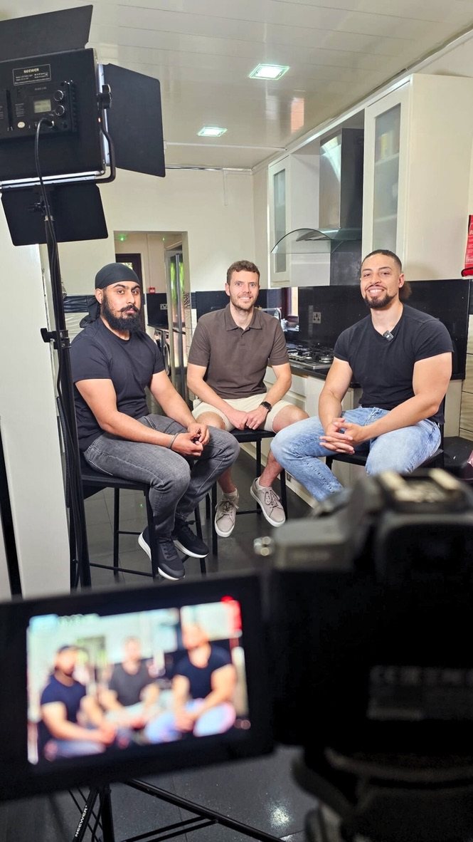 Three people being filmed on set, seen from behind the camera